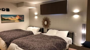 A hotel room with two beds, a large painting of a sunset, a sunburst mirror, and recessed lighting.