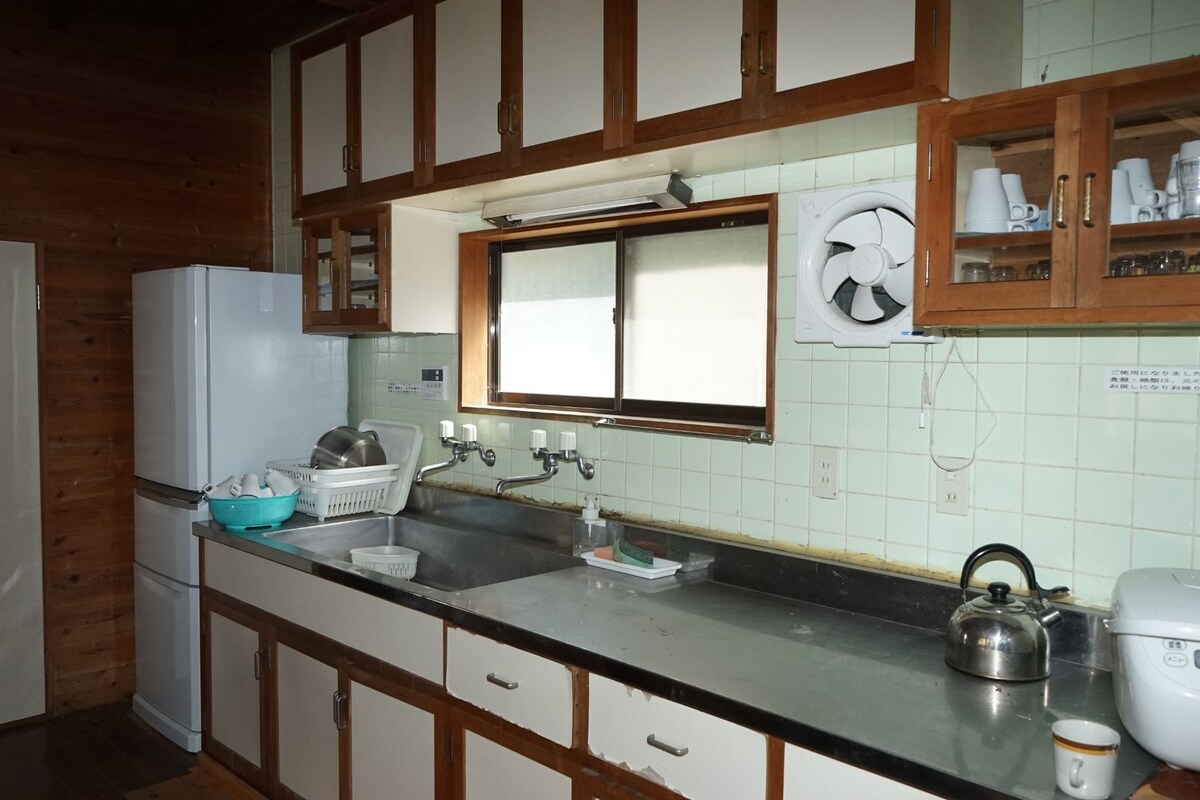 A kitchen with wooden cabinets, a white refrigerator, a sink with a kettle, and a window above the sink.