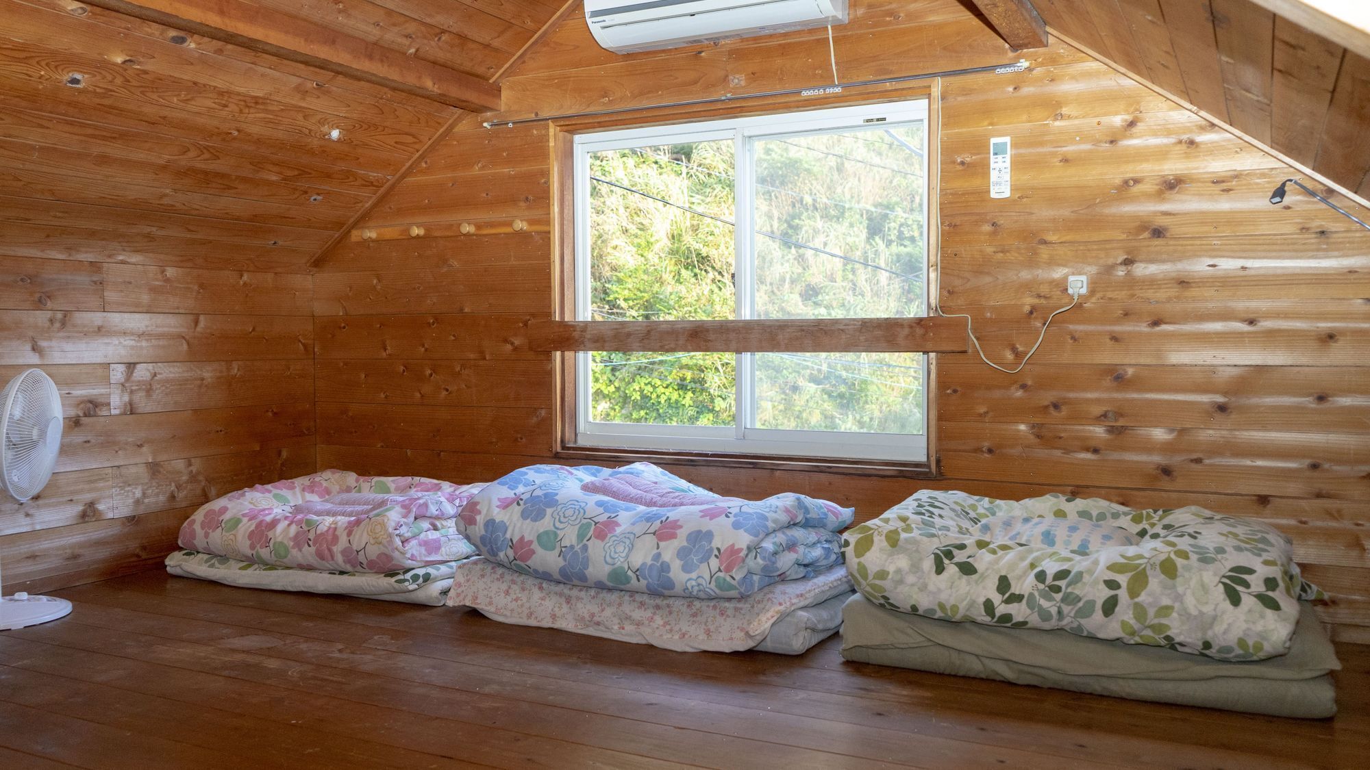 A cozy cabin room with wooden walls, a large window, and three beds with floral bedding.