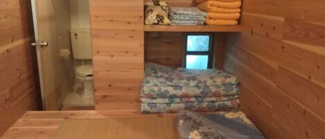 A compact, wooden cabin-style room with a small bed, a toilet, and a window.