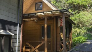 Een houten hut met een veranda, een deur en een bord waarop 'K2' staat.