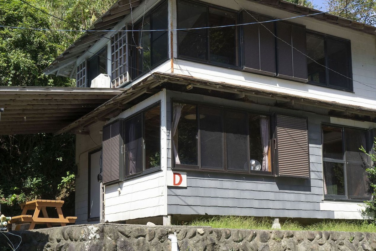 A two-story house with a stone foundation, a wooden deck, and a visible 'D' on the front.