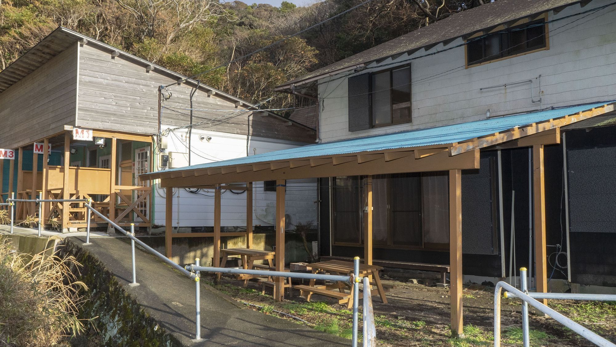 A building with a covered outdoor area, wooden benches, and a small staircase leading to a porch.