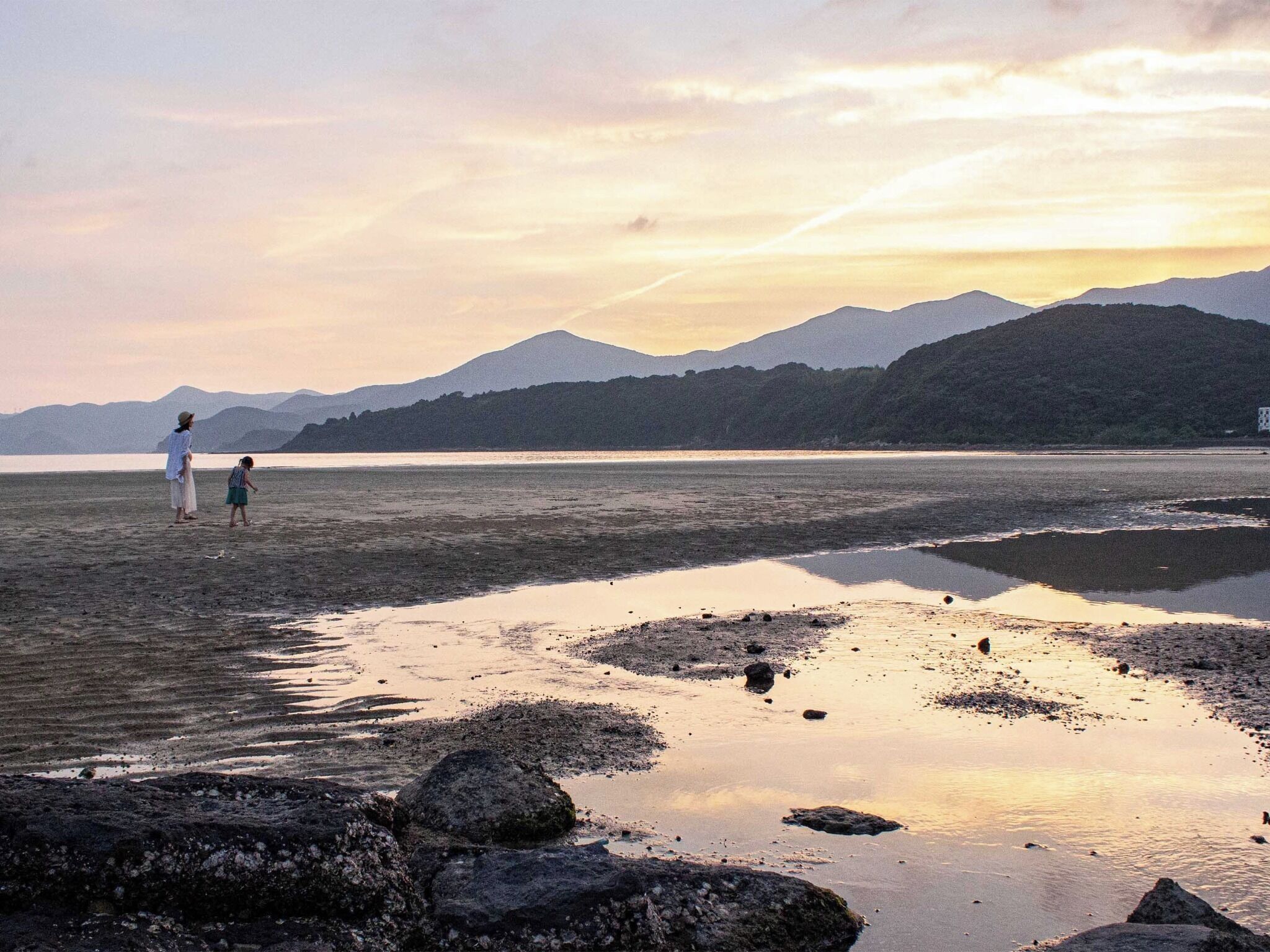 Una spiaggia con un lago calmo, uno sfondo roccioso e montagne sullo sfondo.