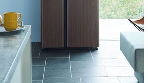 Cocina moderna con un refrigerador doble de madera oscura, una taza amarilla en la encimera y vista a zonas verdes al exterior.