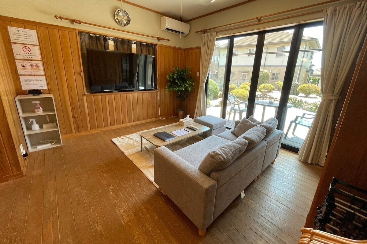 Un salon confortable avec un canapé, un téléviseur à écran plat, des boiseries, une plante et un balcon agrémenté de mobilier d’extérieur.