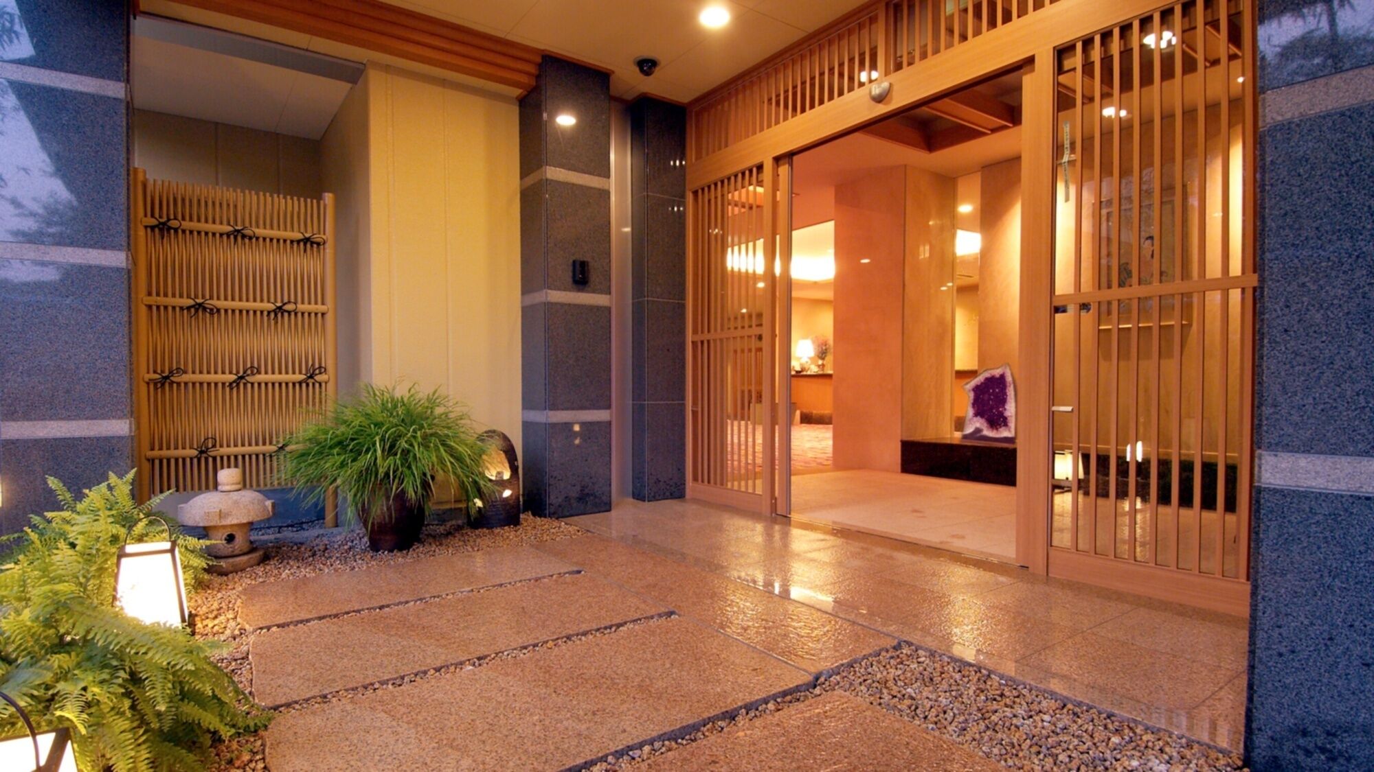 A traditional Japanese-style entrance with sliding doors, a stone lantern, and a small garden area with plants and a stone path.