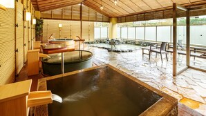 A traditional Japanese onsen with multiple hot tubs, wooden benches, and a stone floor. - Hotel Hamatoku (Iwaki)