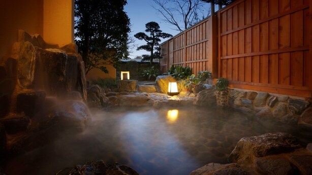 A hot spring area with stone rocks, a wooden fence, and a lit lantern. - Hotel Hamatoku (Iwaki)