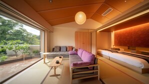 A modern interior with a sofa, a small table, and a bed. There is a window providing a view of greenery outside. - Hotel Hamatoku (Iwaki)