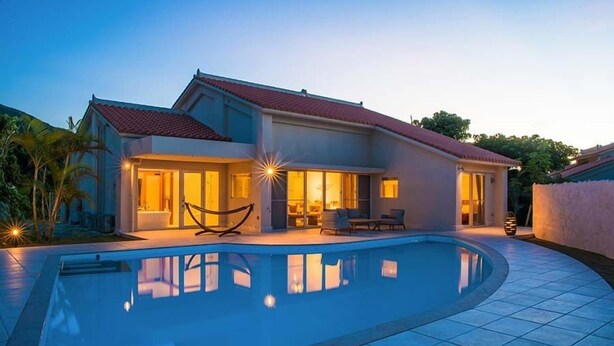 Une maison moderne dotée d’une piscine, de grandes fenêtres et d’un patio bien éclairé.