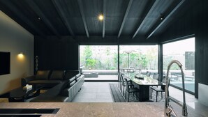 A modern interior with a sofa, dining table, and chairs, large windows, and a kitchen area. - The Goat Awaji (Awaji)