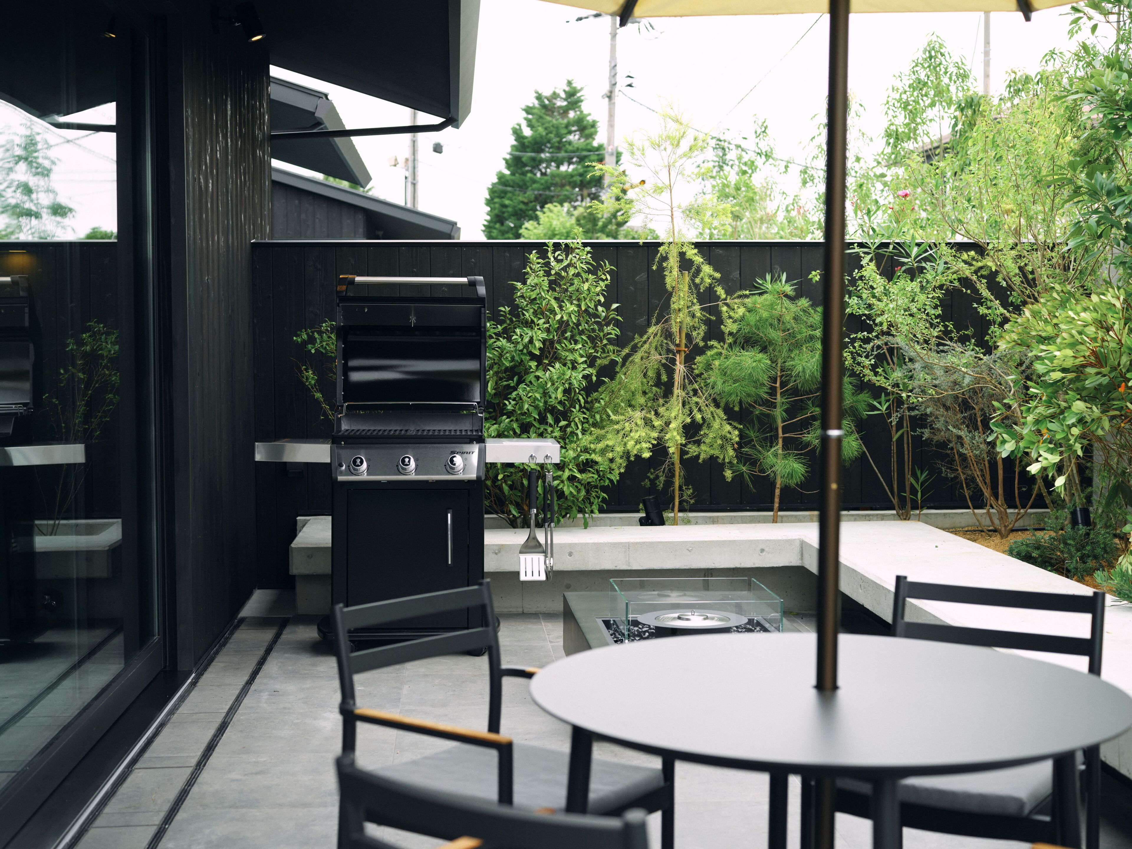 An outdoor patio with a grill, chairs, and a table.