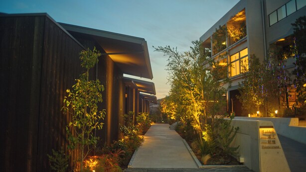 A pathway leading to a building with a modern architectural style, surrounded by greenery and illuminated by warm lighting. - The Goat Awaji (Awaji)