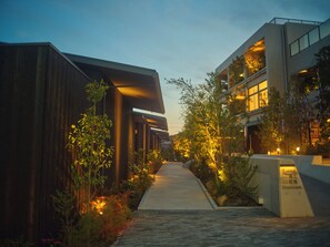 A pathway leading to a building with a modern architectural style, surrounded by greenery and illuminated by warm lighting. - The Goat Awaji (Awaji)