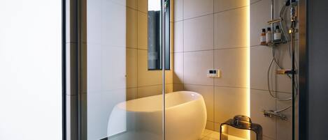 A modern bathroom with a large bathtub, a glass shower enclosure, and a small table with toiletries.