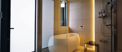 A modern bathroom with a large bathtub, a glass shower enclosure, and a small table with toiletries.