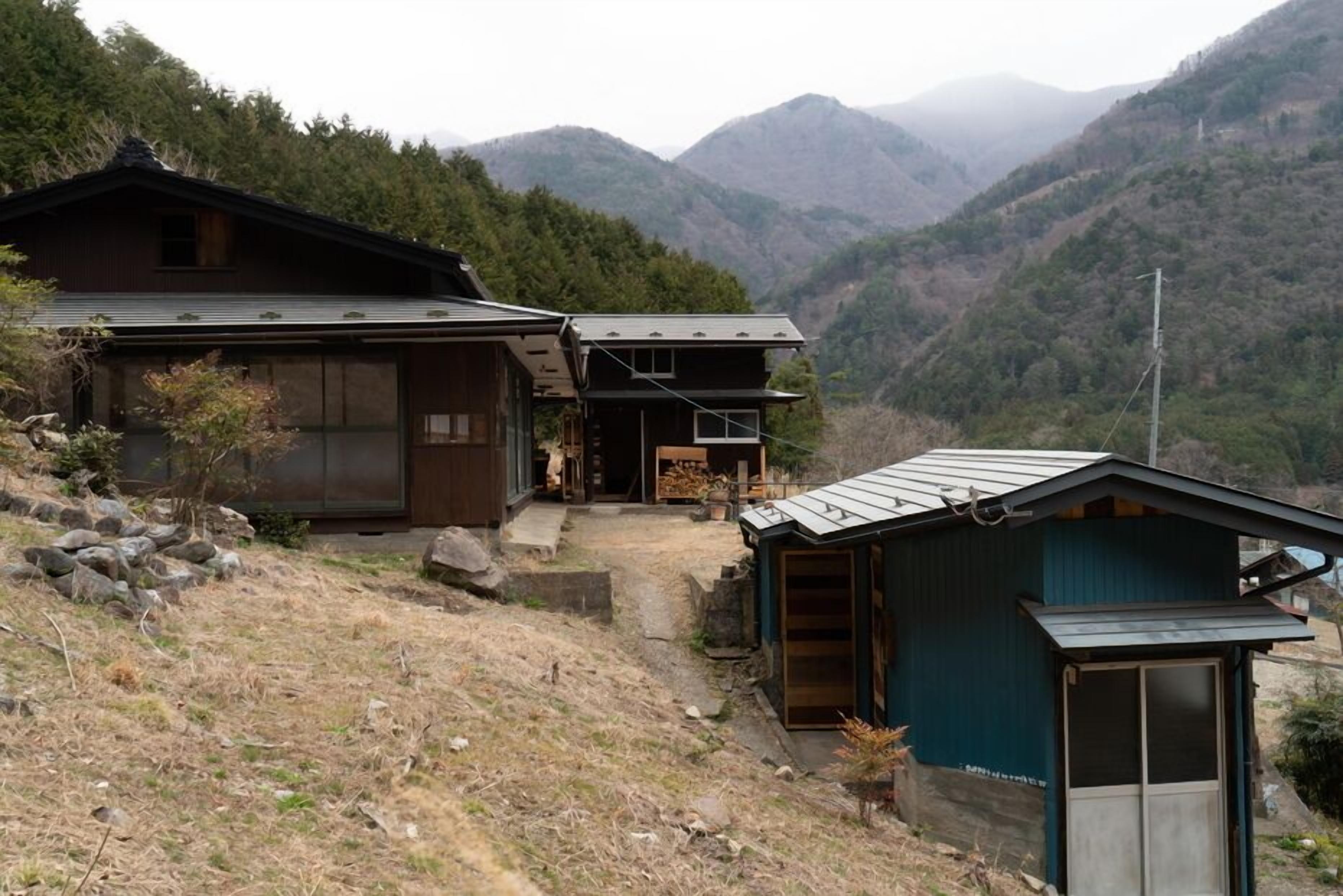 A traditional Japanese house with a wooden exterior, a small attached structure, and a view of mountains in the background.