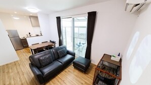 A modern living room with a leather sofa, a wooden floor, and a dining area in the background. - Shipponomori Resort Awajishima Sauna & Studio (Awaji)