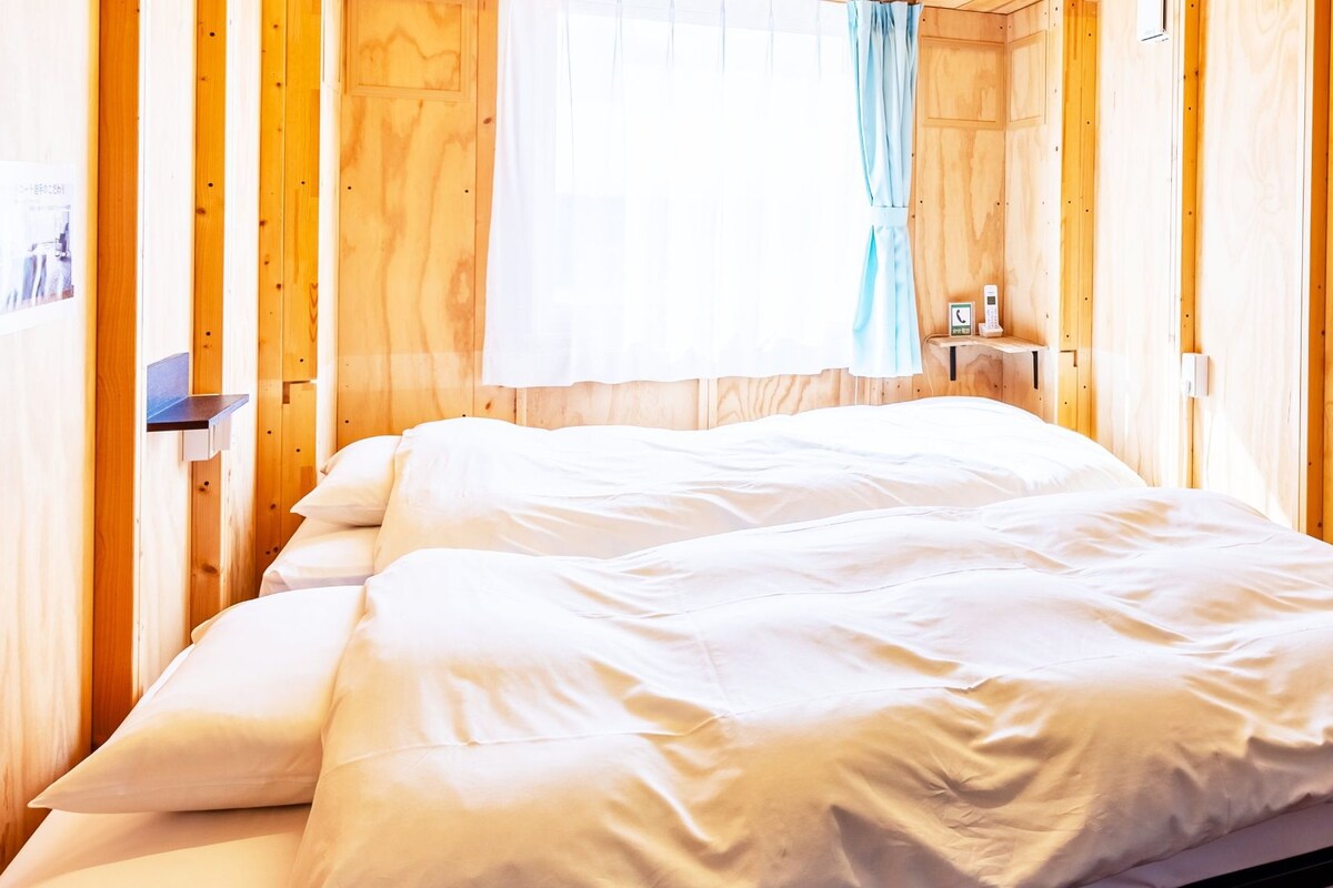 A wooden room with a bed, a nightstand, and a window with curtains.