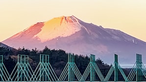 Una montaña con una base boscosa y un puente con barandillas verdes al frente.