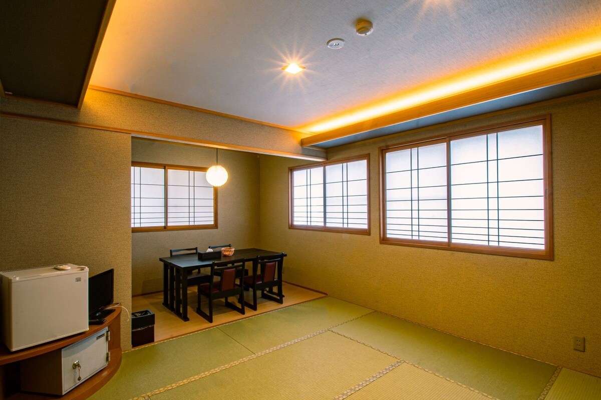 A traditional Japanese-style room with tatami flooring, a low table with chairs, and sliding shoji screens.
