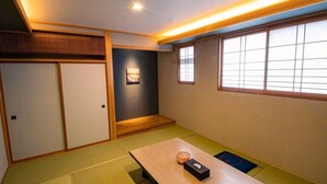 Et traditionelt japansk rum med tatamimåtter, et lavt bord med pude, skydedøre og et vindue med et gittermønster.