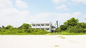 A beachfront building with multiple floors, surrounded by dense greenery. - Uminchuno Yado (Nago)