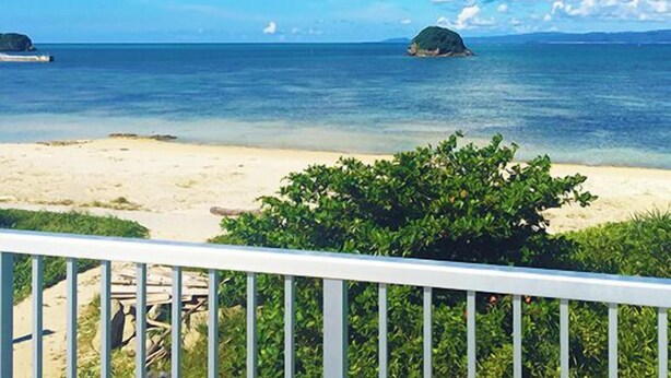 A beach with clear blue water, a sandy shore, and a small island in the distance. - Uminchuno Yado (Nago)