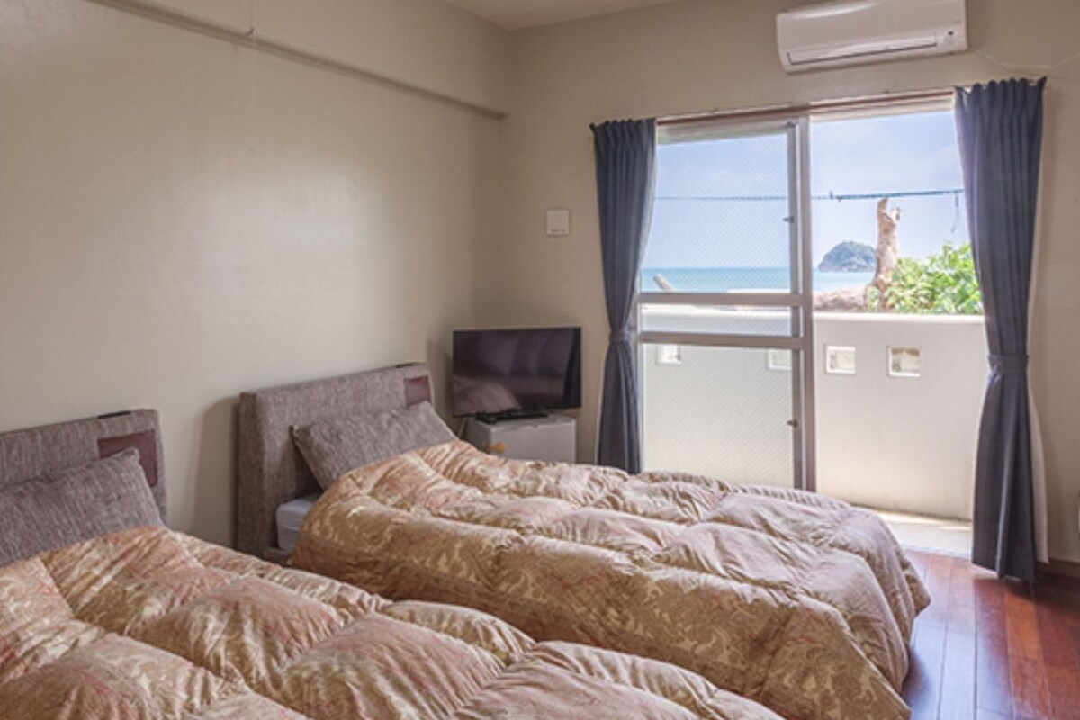 A hotel room with a bed, a television, and a balcony with a view of the sea.
