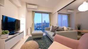 A modern living room with a flat-screen TV, a sofa, a coffee table, and a large window with a city view. - Best Price Kochi (Kochi)
