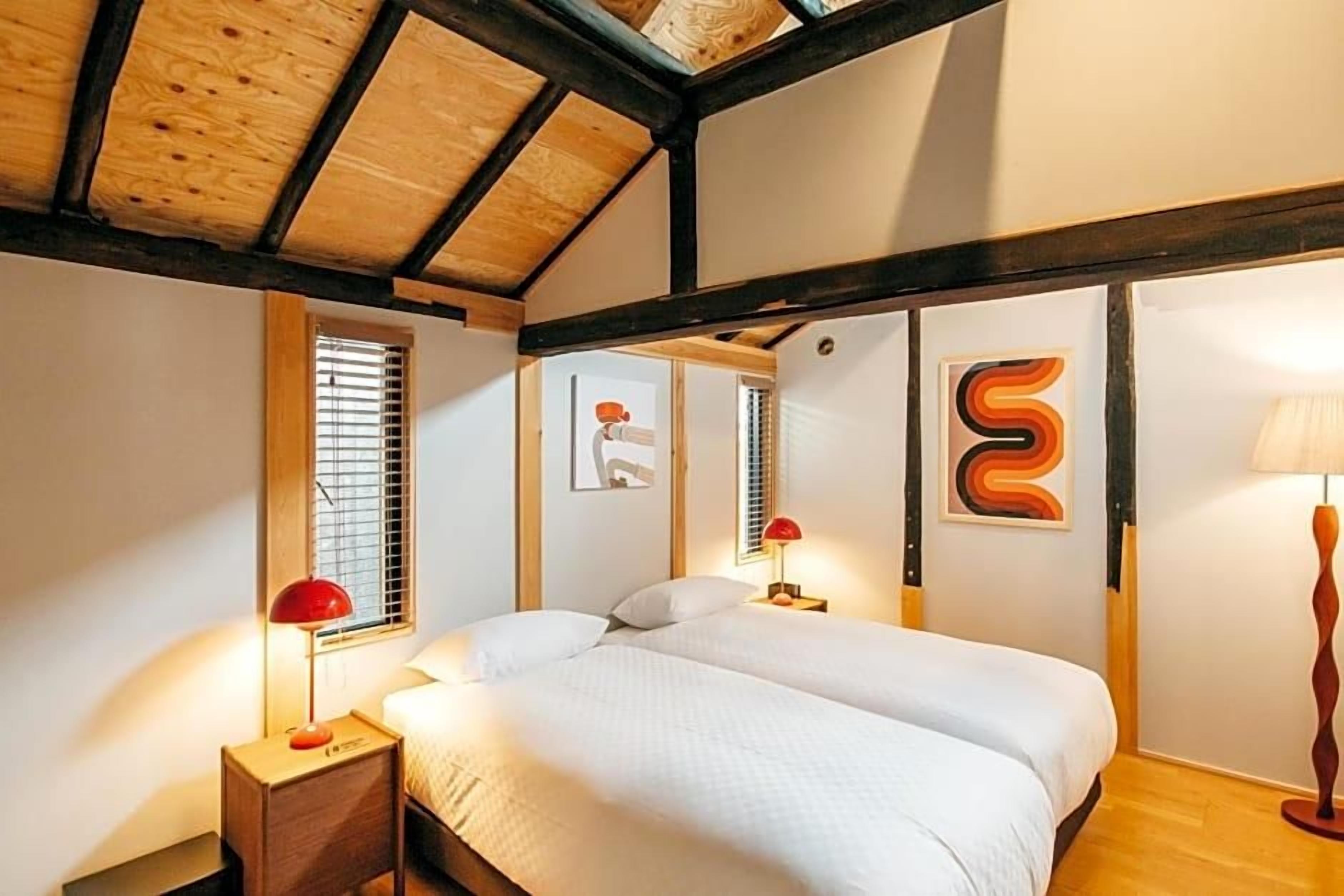 A bedroom with a wooden ceiling, a bed with white bedding, two bedside tables with lamps, and artwork on the walls.