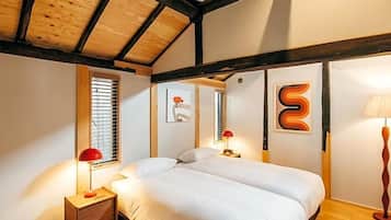 A bedroom with a wooden ceiling, a bed with white bedding, two bedside tables with lamps, and artwork on the walls.