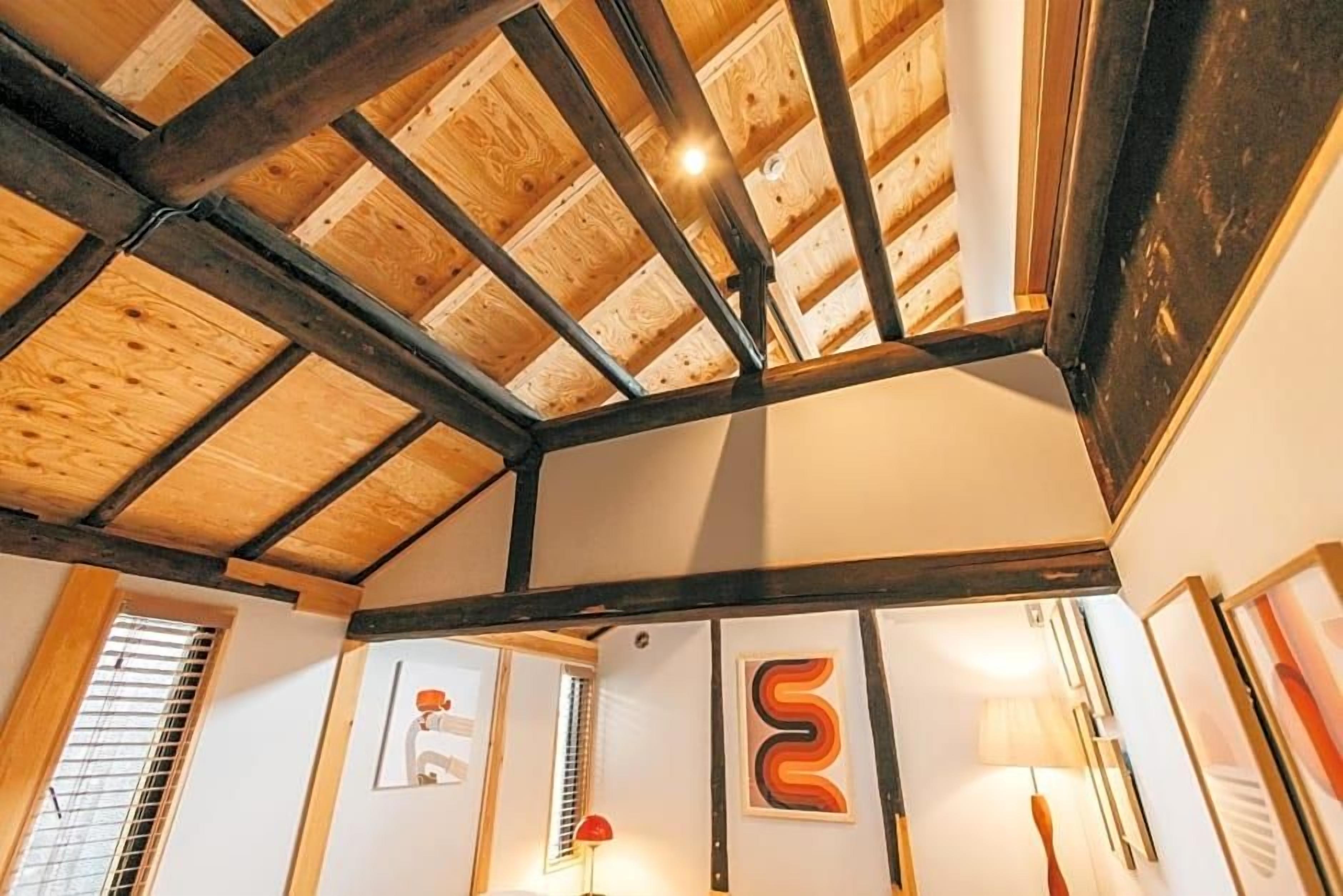 Una habitación con vigas de madera a la vista, techo inclinado y obras de arte en las paredes.