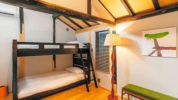 A bunk bed room with a wooden floor, a ladder, a bench, a lamp, and a wall art piece.