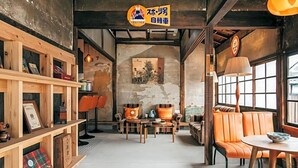 A cozy cafe interior with wooden shelves, orange leather seating, and a vintage poster on the wall. - Yado Charinko (Gose)