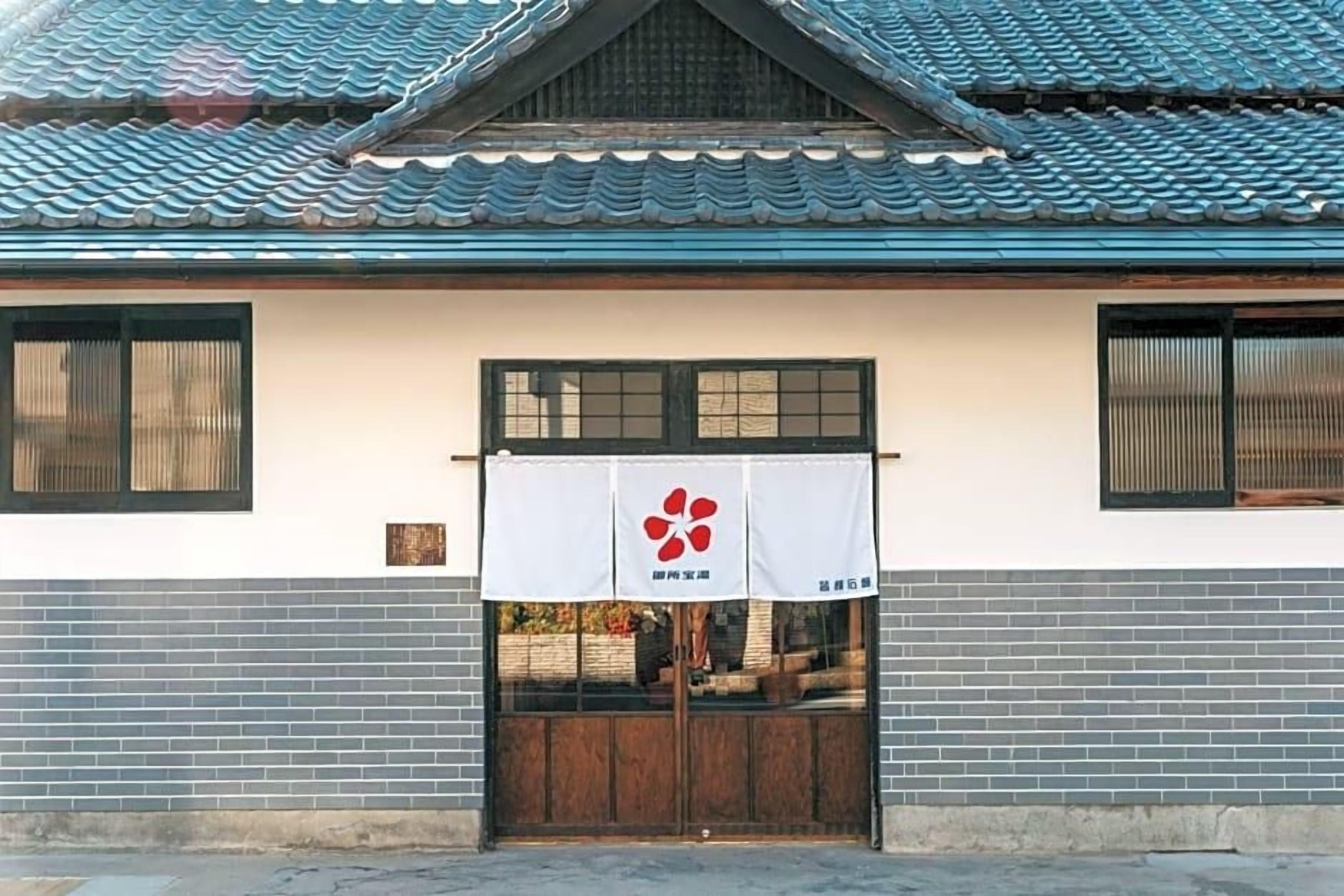 A traditional building with a tiled roof, a wooden door, and a white banner with a red logo.