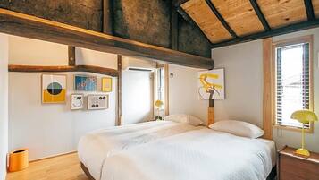 A bedroom with a large bed, wooden beams, a window with blinds, and wall art.