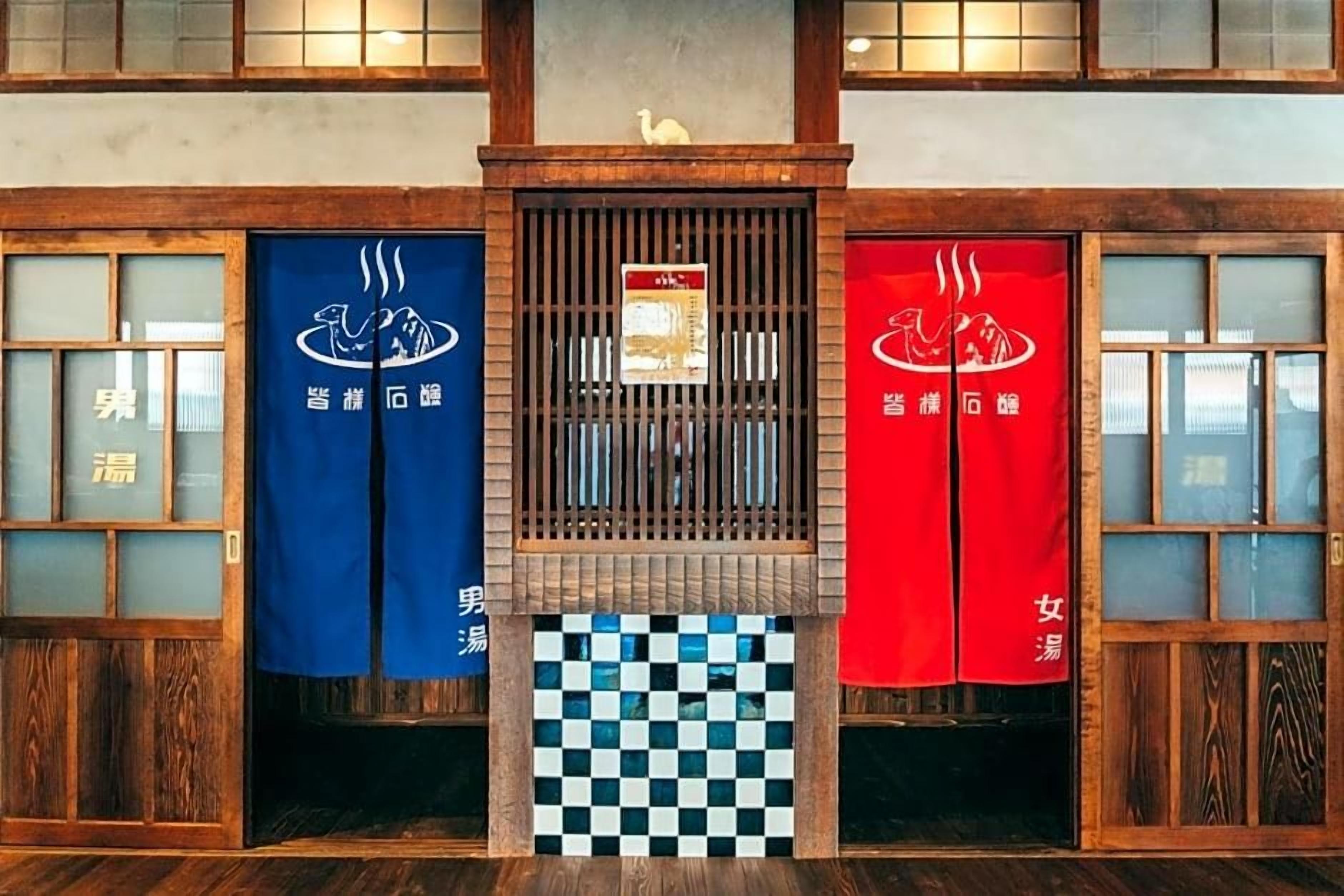 A traditional Japanese-style entrance with two doors, one blue and one red, each with a logo and text indicating separate areas for men and women.