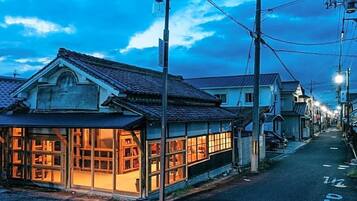 A traditional Japanese building with large windows and a tiled roof, located on a narrow street with other residential buildings.