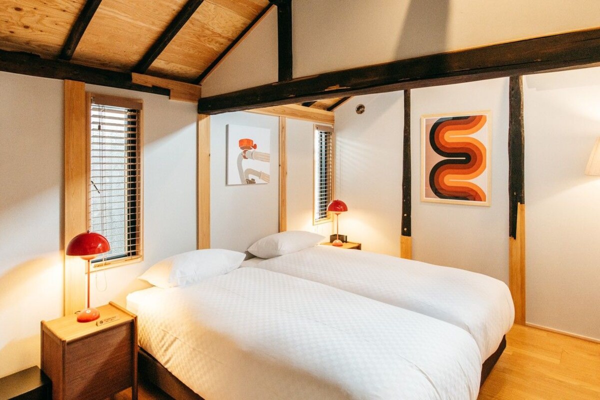 A bedroom with a wooden ceiling, two beds, bedside lamps, and artwork on the walls.