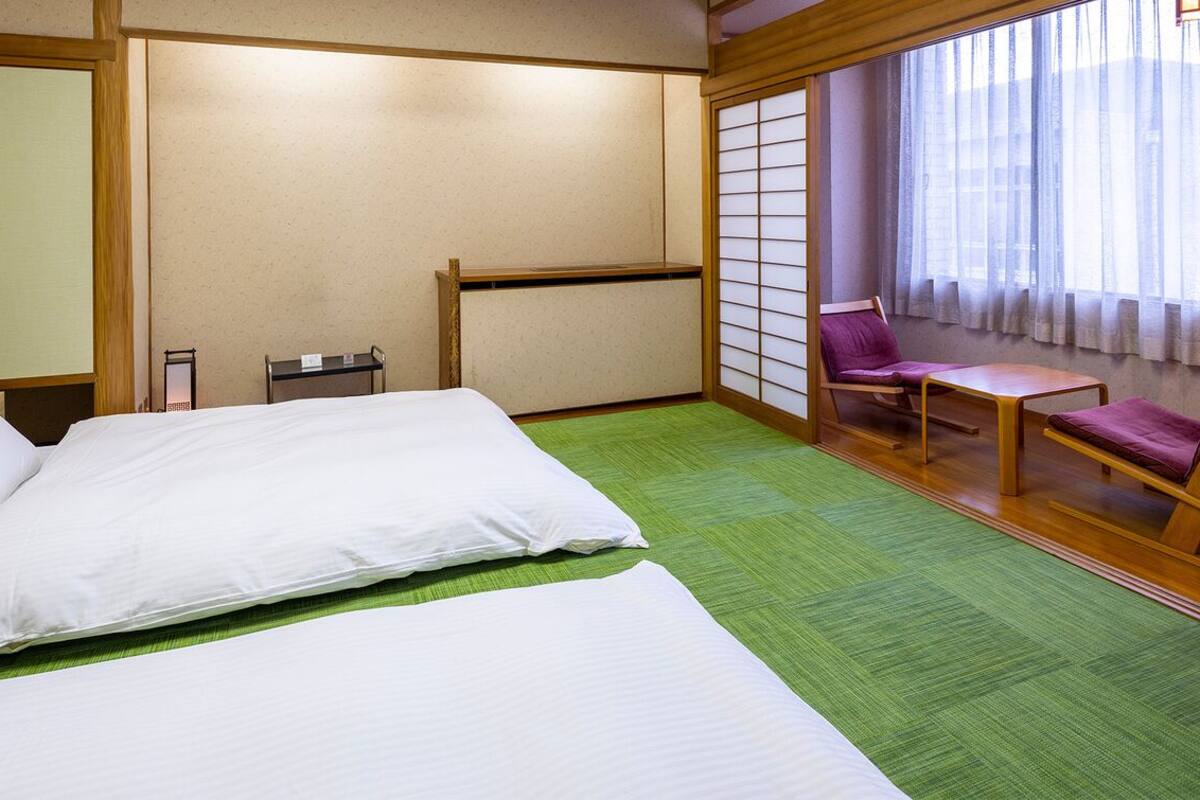 Une chambre d’hôtel avec un lit, un bureau, une chaise et une vue à travers un paravent japonais.