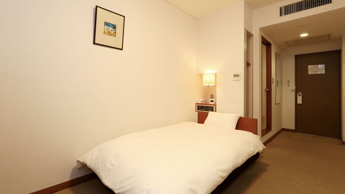 A hotel room with a bed, a nightstand, a lamp, a door, and a framed picture on the wall.
