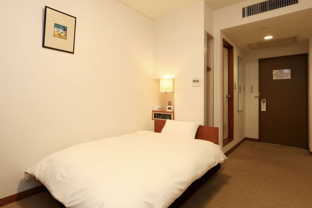 Une chambre d’hôtel avec un lit, une table de chevet, une lampe, une porte et un tableau encadré au mur.
