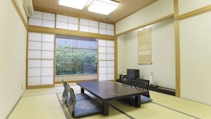 Um quarto japonês tradicional com tatames, uma mesa baixa e vista para o verde lá fora.