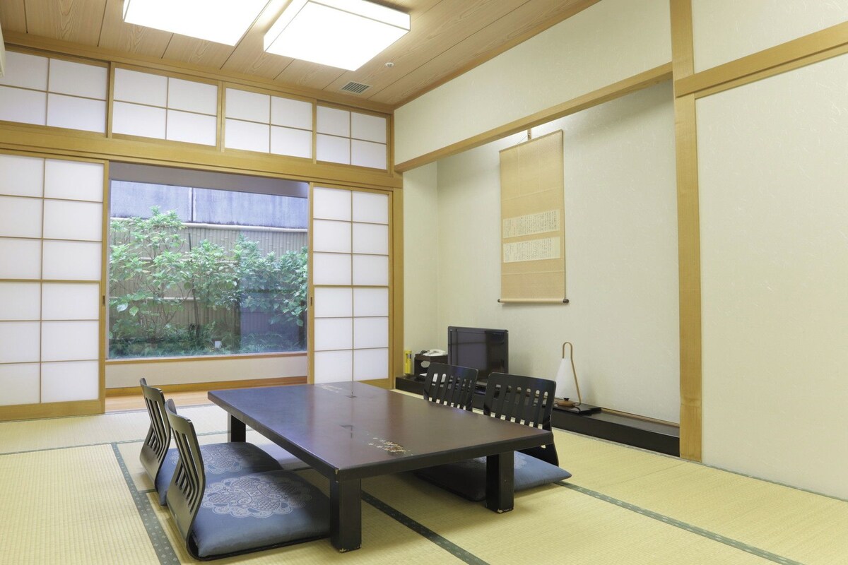 A traditional Japanese room with tatami flooring, a low table, and a view of greenery outside.
