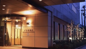 Entrada de edifício com placa em japonês, porta de vidro e árvore com luzes.