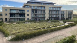 A modern multi-story building with balconies, a landscaped garden area, and a paved walkway. - Apartment with sunny terrace in Oostduinkerke (OOSTDUINKERKE)