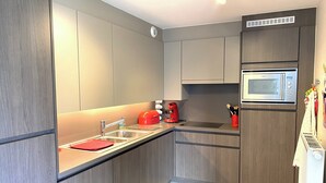 A modern kitchen with grey cabinetry, a stainless steel sink, a red kettle, and a built-in microwave. - Apartment with sunny terrace in Oostduinkerke (OOSTDUINKERKE)