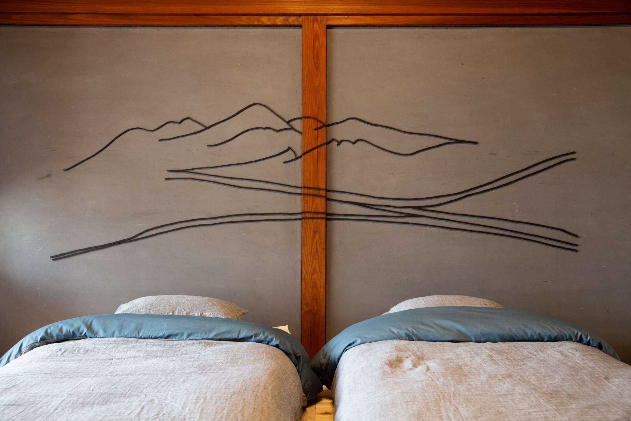 Un dormitorio con dos camas, cabeceros de madera y una pared decorada con un dibujo sencillo de montañas.